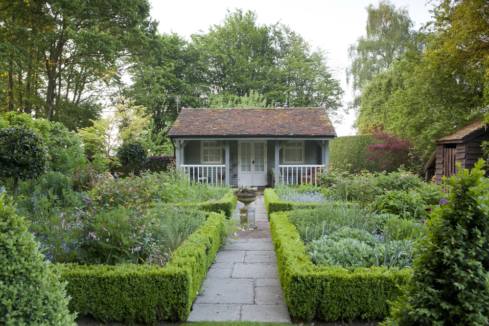 Formal garden with paved walkway between planted areas and summerhouse in the background