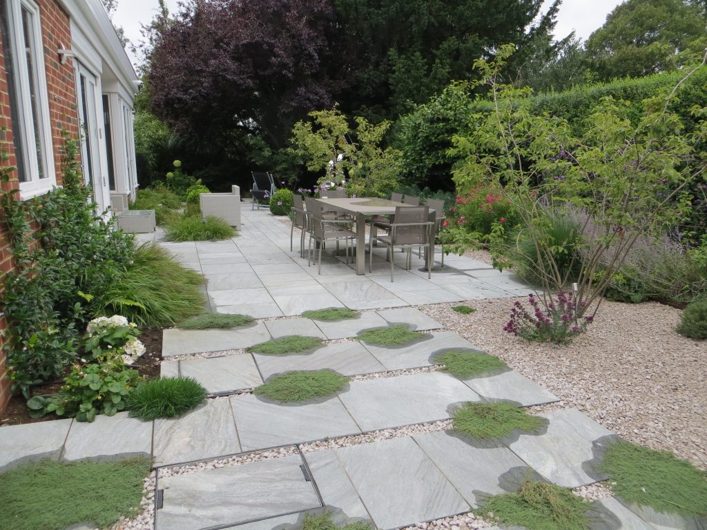 Courtyard garden with paved terrace and dining furniture surrounded by planting